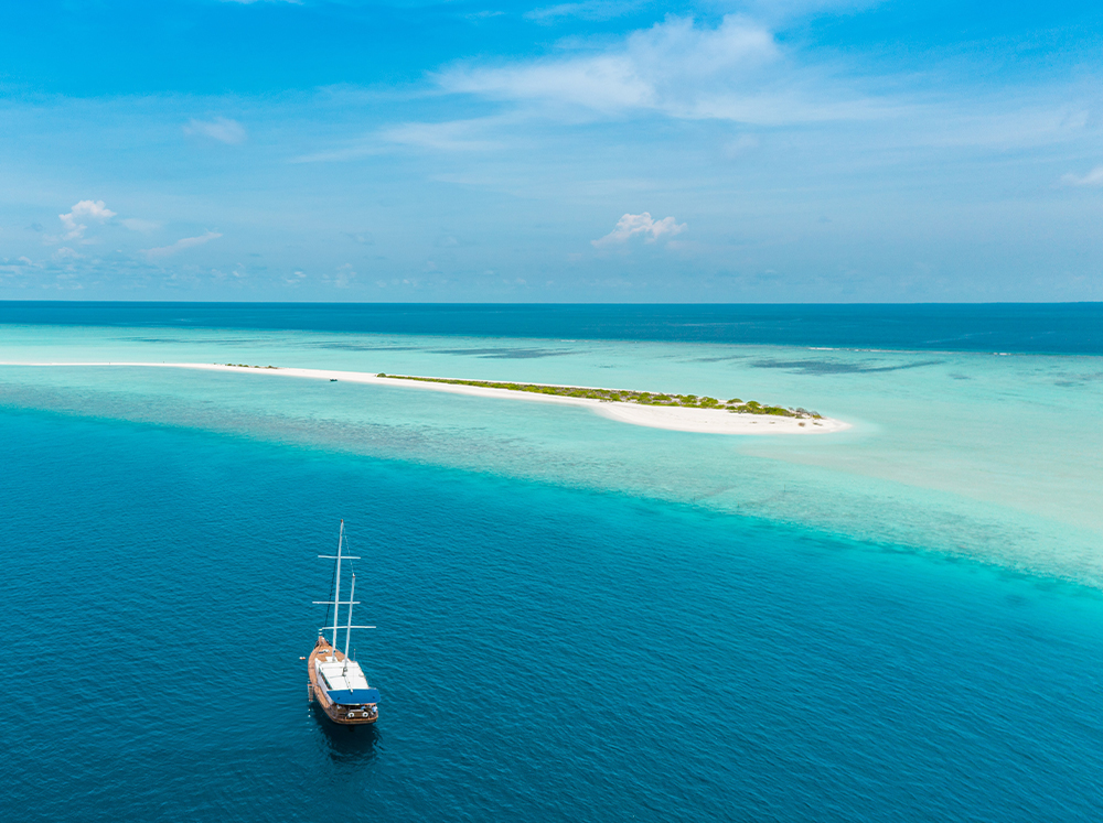 A sailboat anchored near an uninhabited island with crystal clear waters.